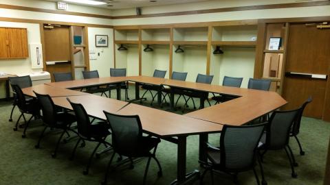 Picture of a meeting space with four tables arraged in a circle surrounded by chairs.